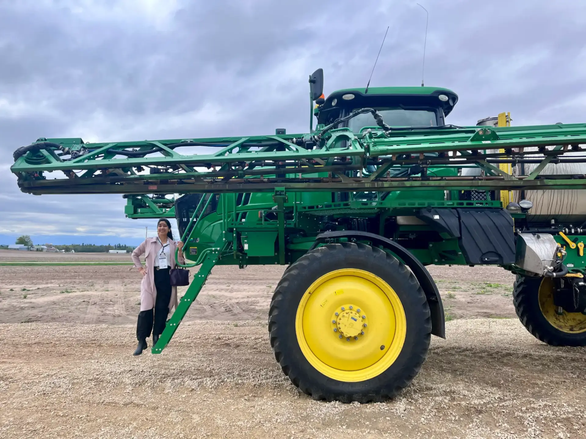 Maddy Kulkarni standing beside a large agricultural sprayer during a farm field visit